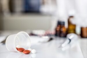 Some pills spillage for a plastic cup with medication bottles in the background.