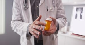 A doctor pointing to a container of pills they are holding.