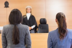 A solicitor and their client standing in front of a judge in a courtroom.