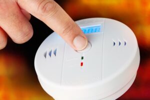 A person's finger on the test button for a carbon monoxide alarm.
