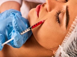 A woman with a syringe of red liquid on her cheek. 