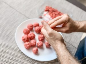 Someone preparing raw mince meat balls on a white plate.