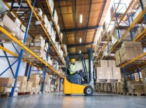 A worker inside a warehouse moves boxes while driving a forklift