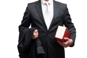 Torso shot of a train accident lawyer in a suit holding a red law book in one arm and his blazer in the other. 