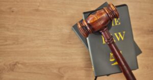 A gavel on top of a black law book on an oak table. 