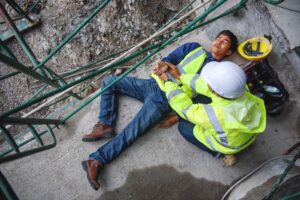 A in a high vis jacket being attended by his colleague after suffering scaffolding injuries