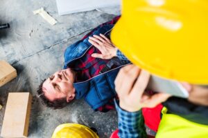 a construction worker laying on the ground after a workplace accident while a colleague provided first aid.