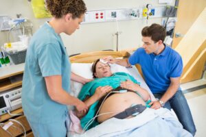 A woman prepares to give birth in a hospital bed. A man and midwife are in attendance. 