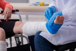 A doctor dresses the left leg of a wheelchair user is white and blue bandages.