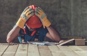 Man in a hardhat and gloves with his hands over his head. 