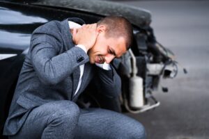 PERSON WITH NECK INJURY CROUCHING BY HIS CAR AFTER AN ACCIDENT