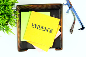 The word 'evidence' written on a yellow post it note in a basket next to a plant and glasses. 