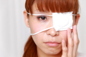 A woman with a medical patch over her eye, touching her face