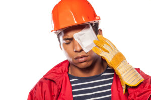 A construction worker with a patch over his eye reaching up to touch his face