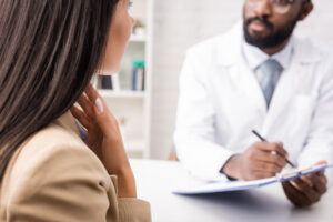 A woman touches her throats while a doctor takes notes.