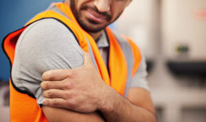 A worker in a hi-vis vest winces in pain as he holds his arm.