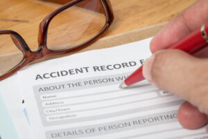 An employer completing an accident record with a red pen. A pair of glasses have been placed on the table